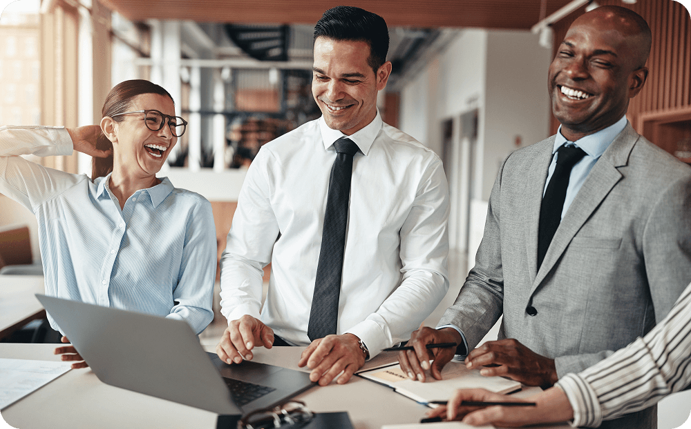 Three people standing around a table with a laptop on it.